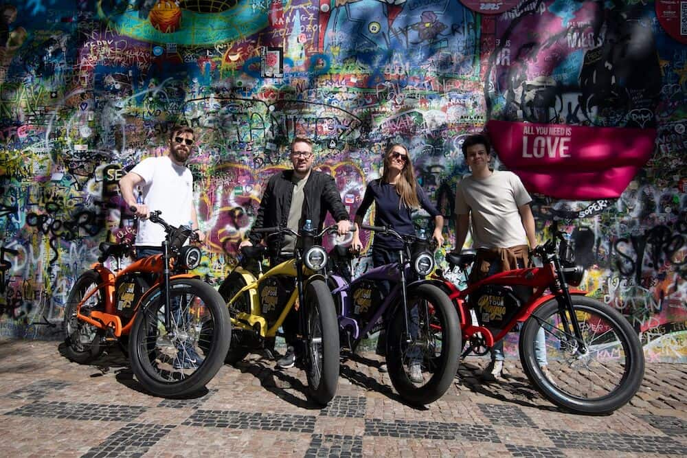 Grupp åkare med café-racer-e-bikes vid Lennonmuren i Prag