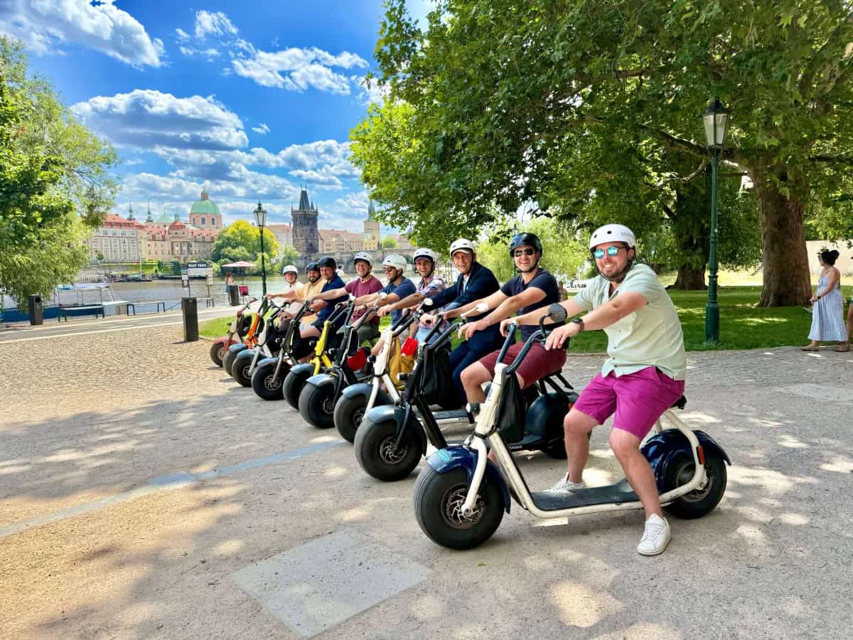 Skupina jezdců na SCROOSER e-koloběžkách u Vltavy s Karlovým mostem v pozadí